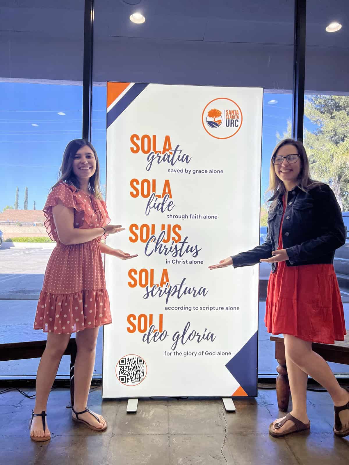 Two members of Santa Clarita United Reformed Church beside a banner displaying the Five Solas of the Reformation